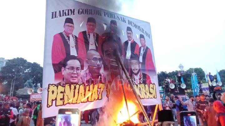 Massa aksi Hari Buruh Internasional membakar baliho bergambar Presiden Joko Widodo dan sejumlah pejabat negara lainnya di kawasan Patung Arjuna Wijaya, Jakarta Pusat pada Rabu, 1 Mei 2024.